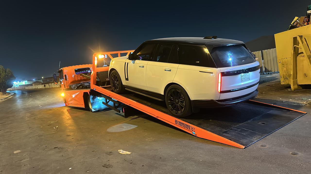 سطحة برتقالية تحمل رينج روفر أبيض في الليل